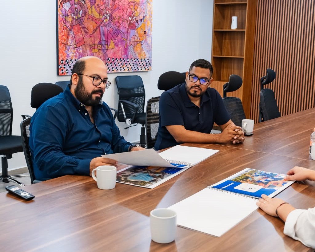 Dos hombres sentados a una mesa durante una reunión de trabajo, con documentos y fotografías sobre el proyecto.